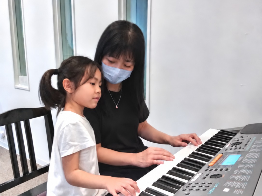 講師と子どもが電子ピアノで一緒に鍵盤を弾くレッスン風景