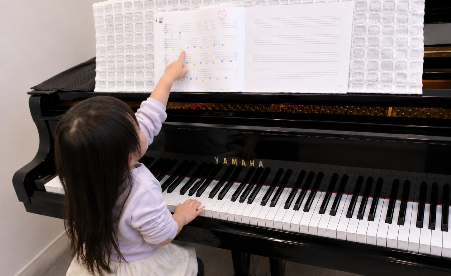 ピアノの前で楽譜を指さしながら学ぶ子どものレッスン風景