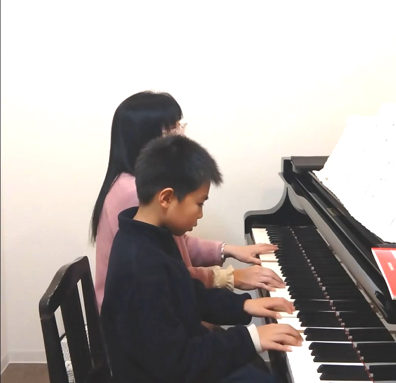子どもと指導者が並び、グランドピアノを弾いているレッスン風景
