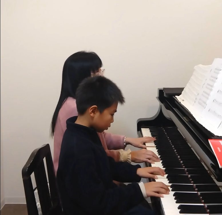 講師が子どもの手元を見ながらピアノを指導している様子